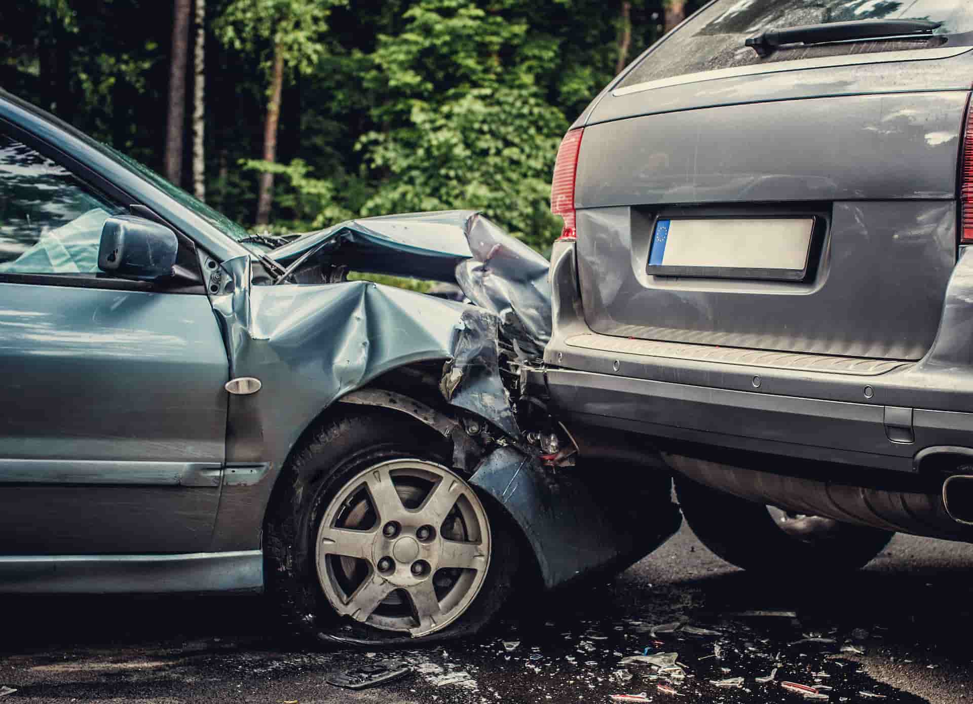 A light blue-green car with a crumpled front end and flat tire after rear-ending a grey SUV.