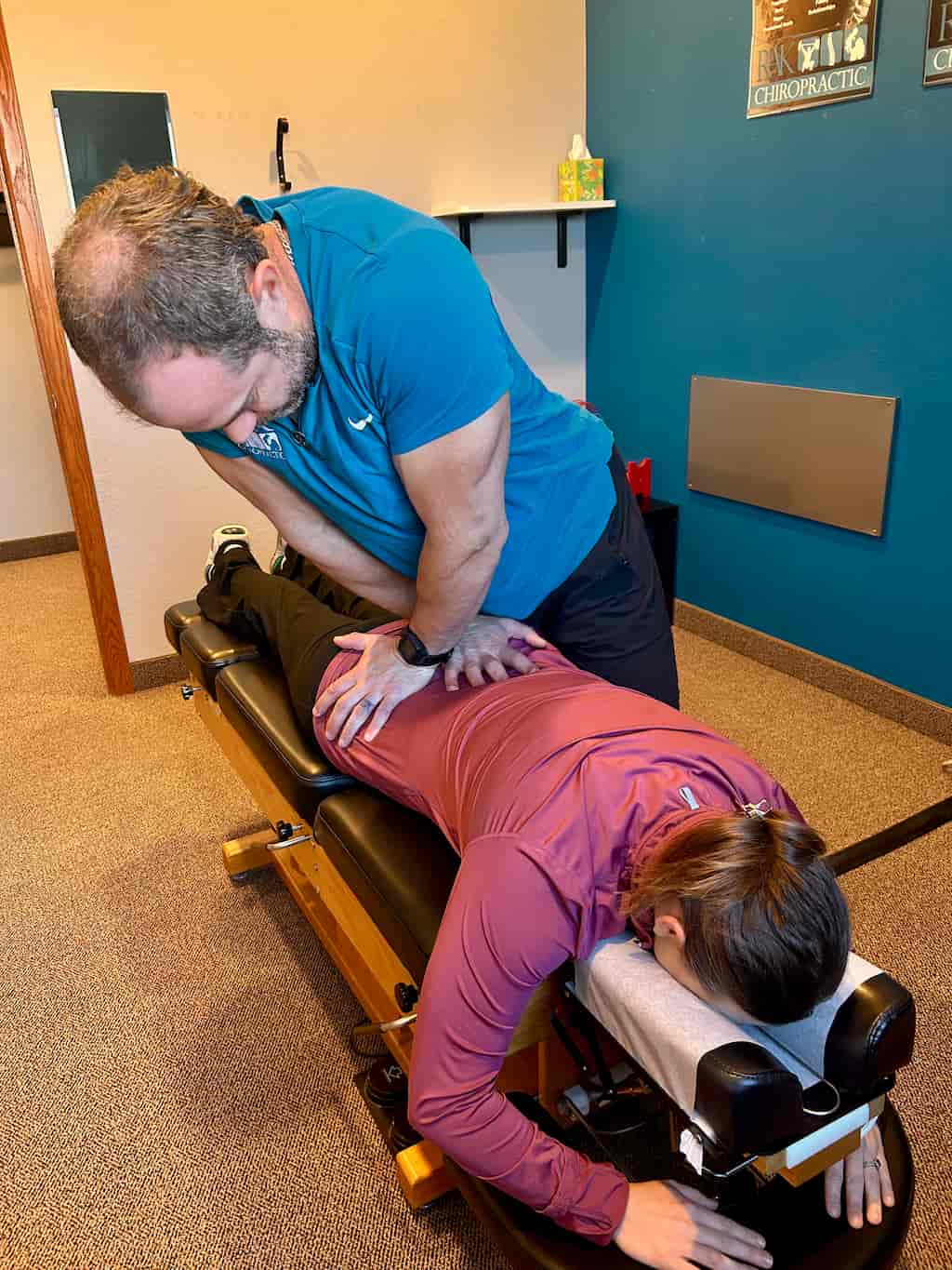 A male chiropractor adjusts the lower back of a female patient lying face down on a chiropractic table.