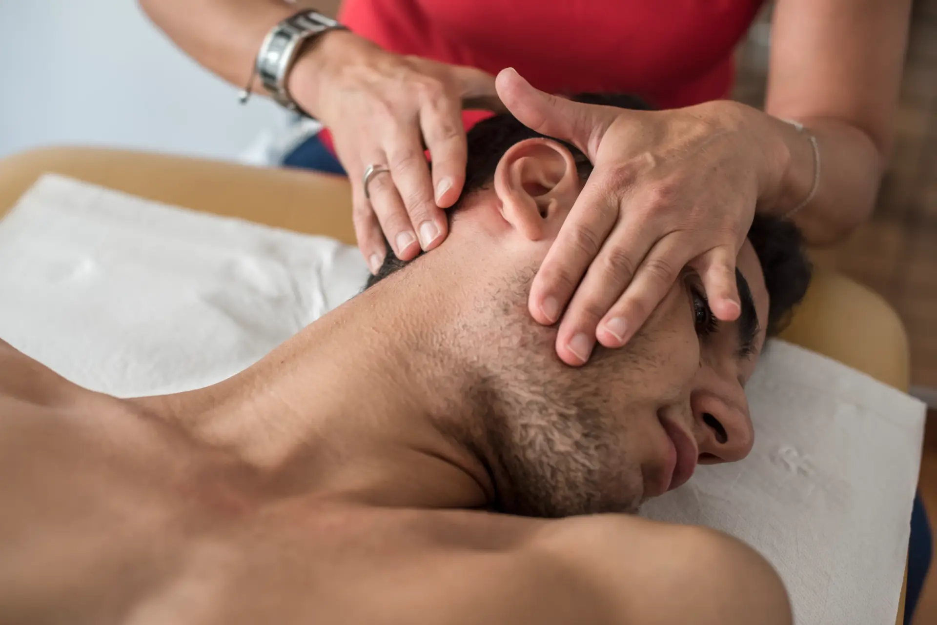Close-up of a person lying face down, receiving a head and neck massage from a masseuse.