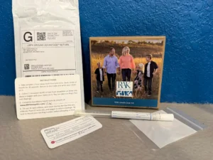 A RAK Health Scan Kit, including a box with a family photo, a USPS return envelope, instruction card, ID card, swab, and plastic baggie, laid out on a gray surface.