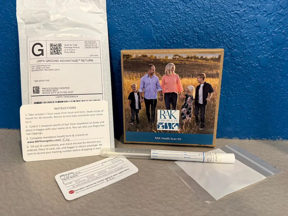 A RAK Health Scan Kit, including a box with a family photo, a USPS return envelope, instruction card, ID card, swab, and plastic baggie, laid out on a gray surface.
