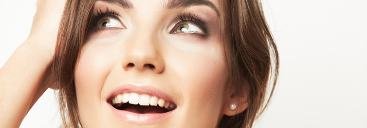 Close-up of a smiling woman with brown hair and green eyes looking upwards, wearing a pearl earring.