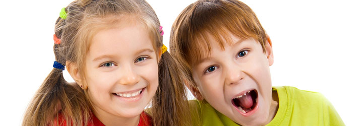 A smiling young girl with pigtails and a boy with an open mouth, both looking at the camera against a white background.