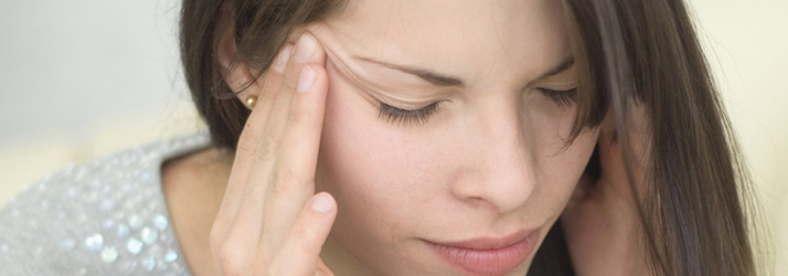 Close-up of a woman with closed eyes, pressing her hands to her temples, appearing to have a headache.