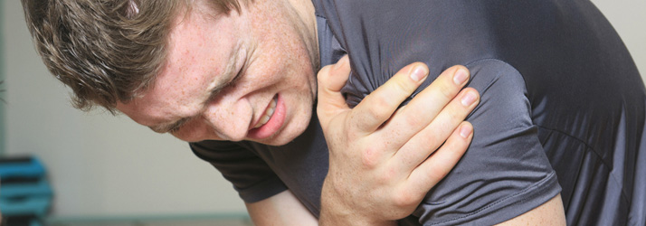 A man grimacing in pain, clutching his right shoulder with his left hand.