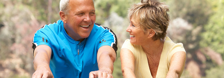 An older man and woman, both smiling, look at each other while outdoors.