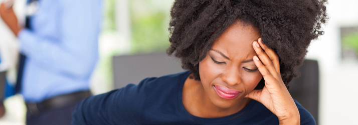 Close-up of a Black woman with curly hair, eyes closed, holding her hand to her forehead in discomfort.