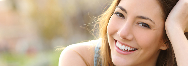 Close-up of a young woman with dark hair smiling broadly, revealing bright white teeth, looking upwards and to the right.